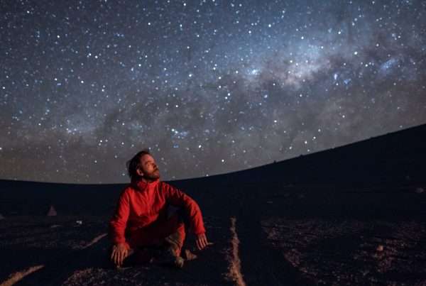 A young adult man seating and looking at the view of our Milky Way galactic core located in the constellation of Sagittarius, an amazing view at Atacama Desert.
